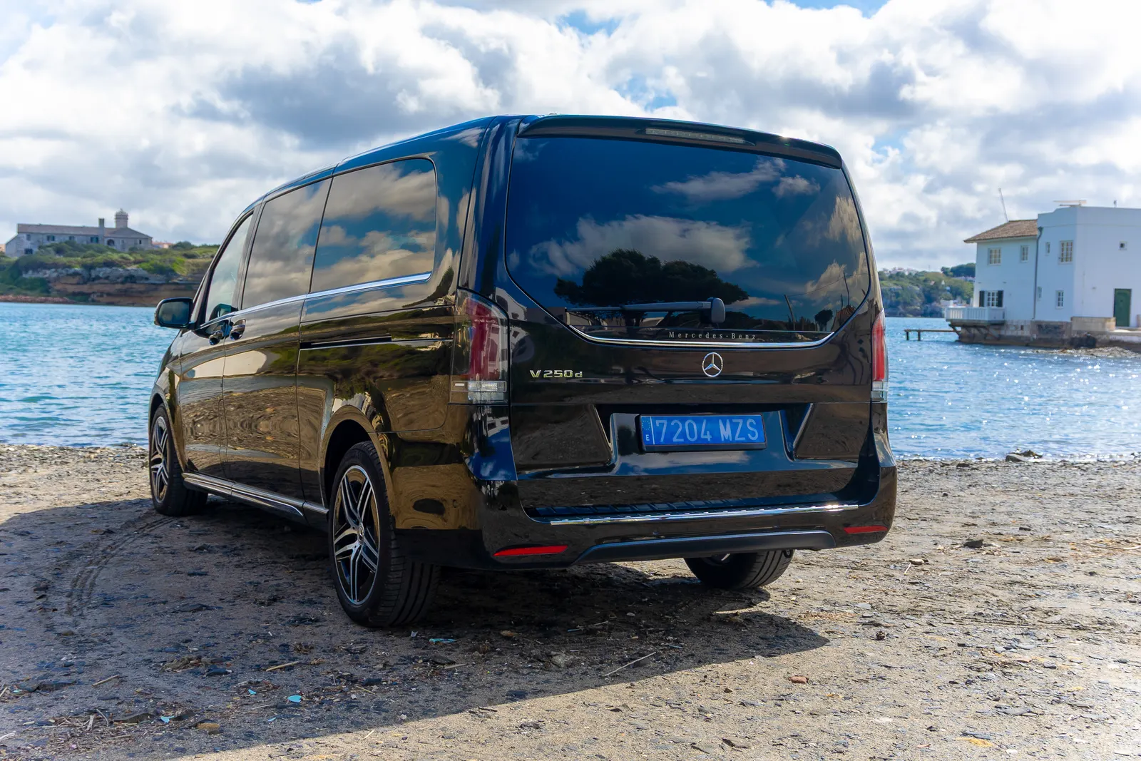 Mercedes Clase V negro de Menorca Bus visto desde atrás junto al agua, con espacio para un grupo de invitados.