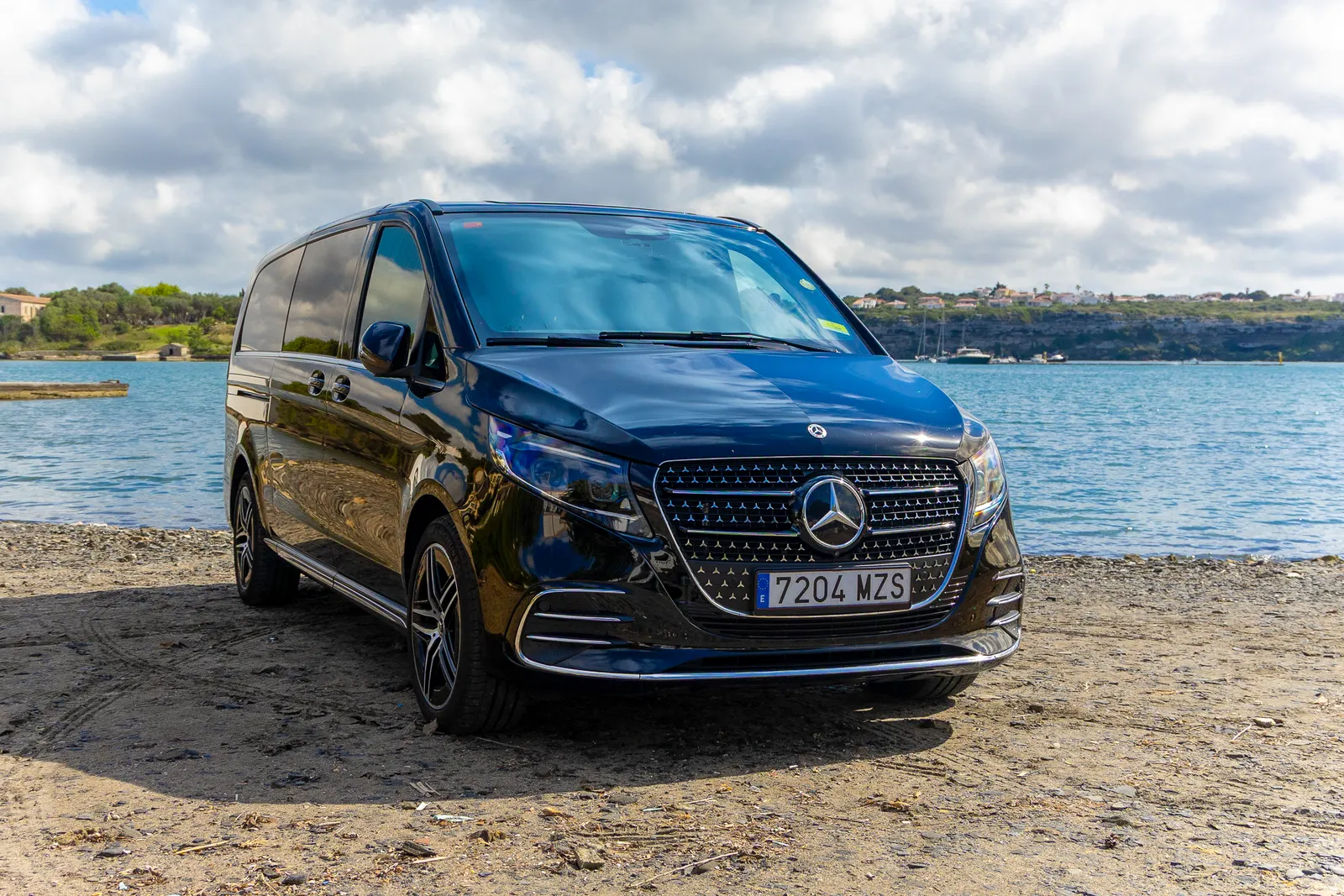 Mercedes Clase V negro de Menorca Bus junto a una bahía de Menorca, listo para una celebración.