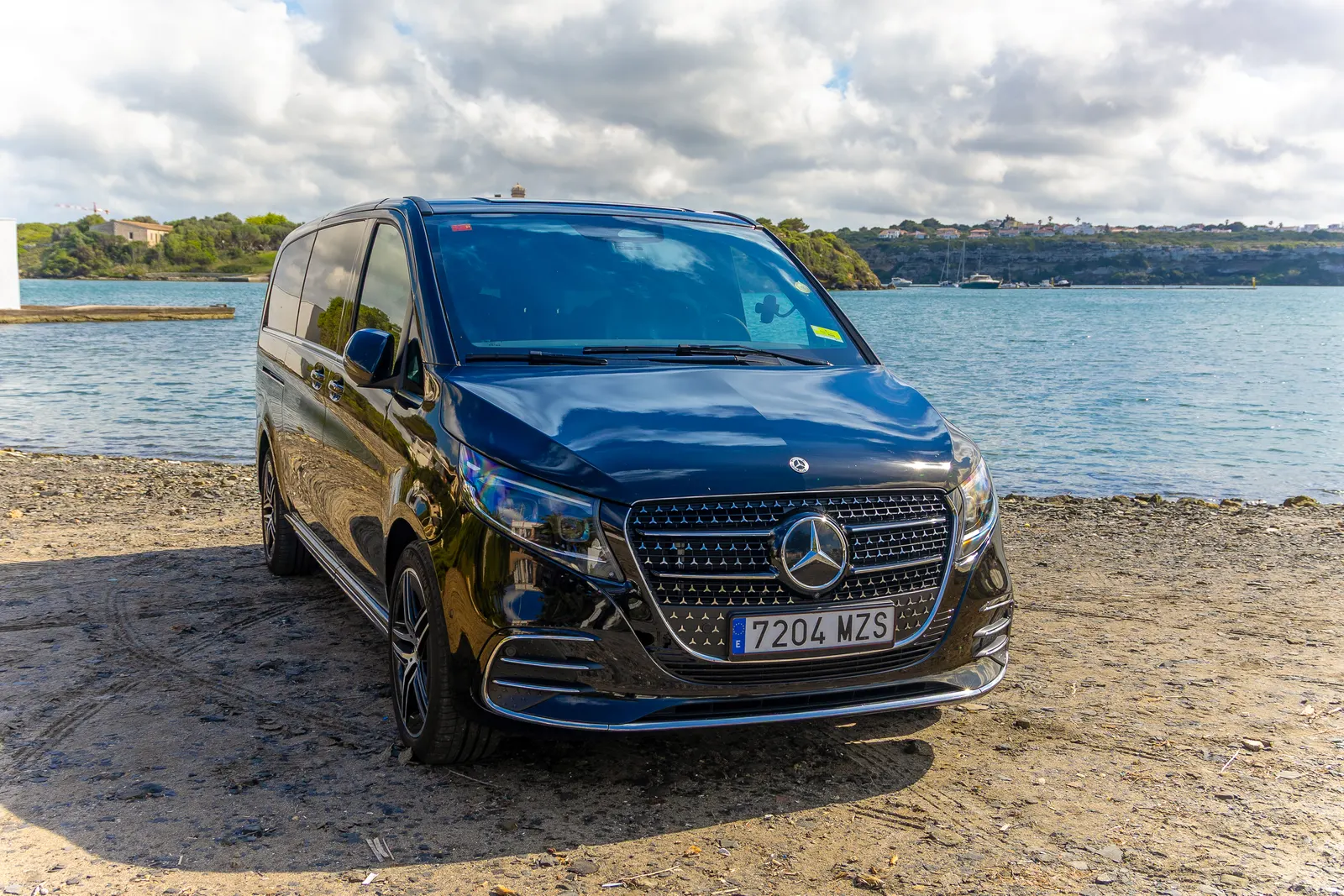Mercedes Clase V negro de Menorca Bus junto a una cala de Menorca, listo para una excursión.