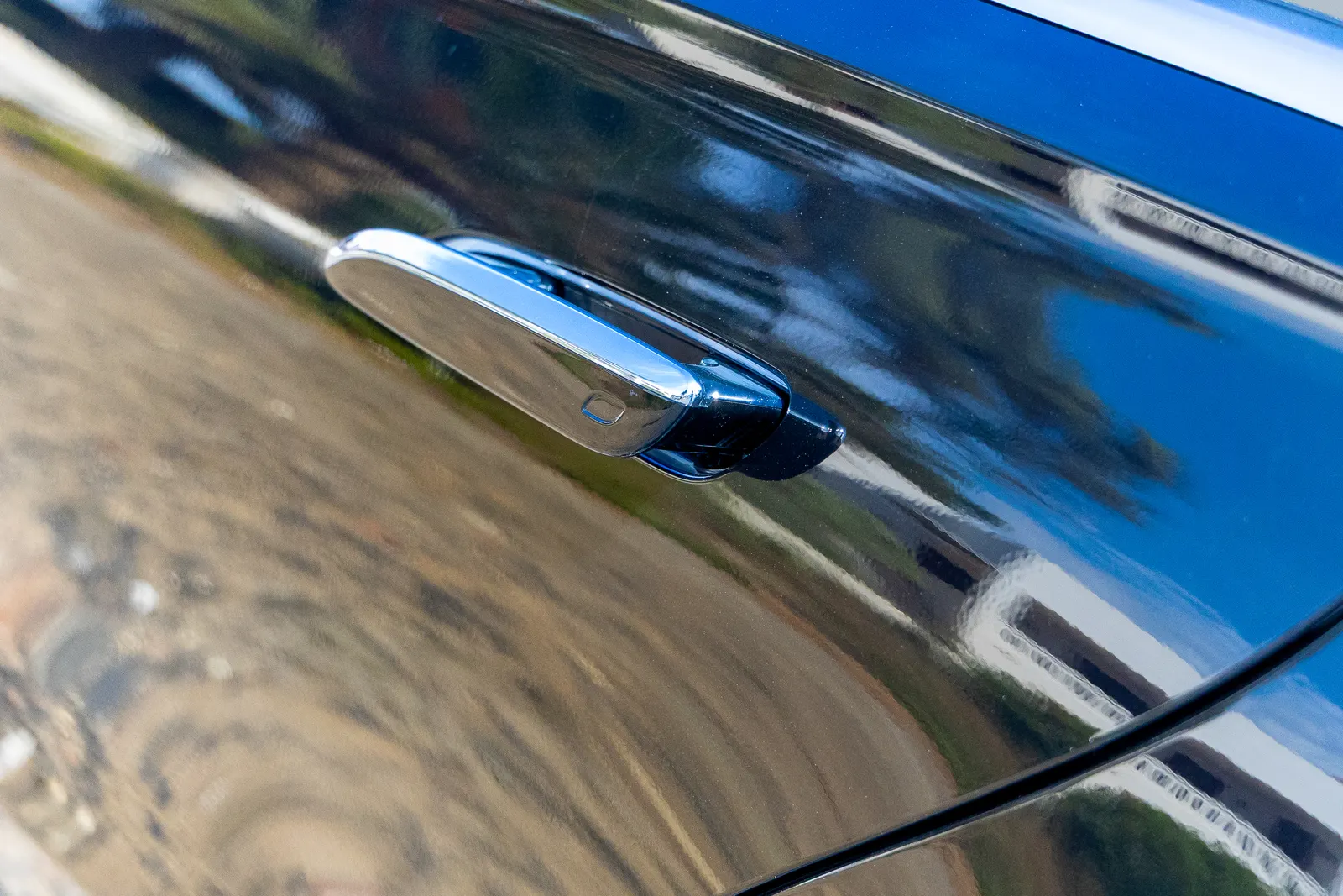 Detalle del tirador cromado de un Mercedes negro reflejando el paisaje de Menorca.