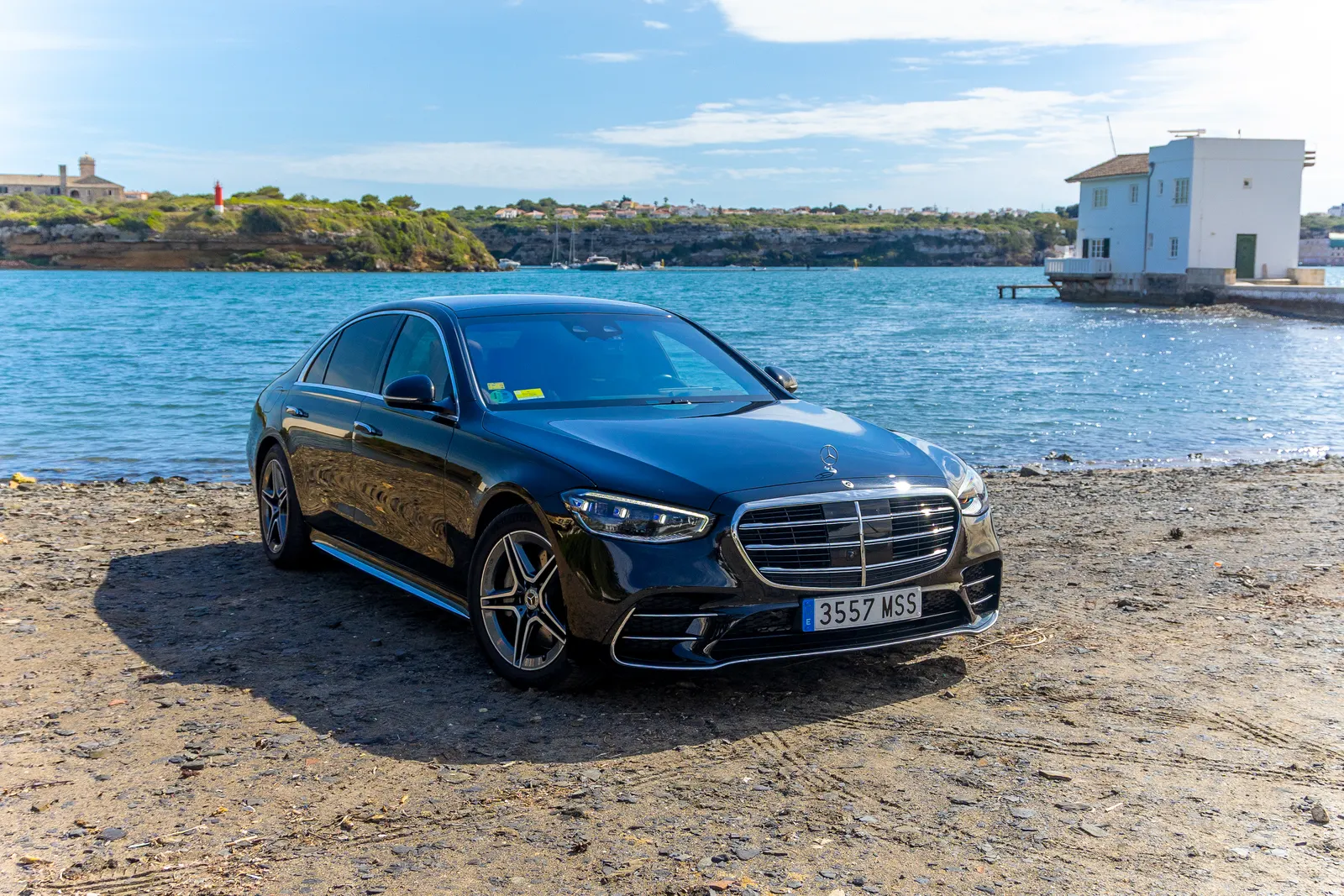 Mercedes Clase S negro de Menorca Bus junto a una bahía de Menorca, con agua turquesa al fondo.