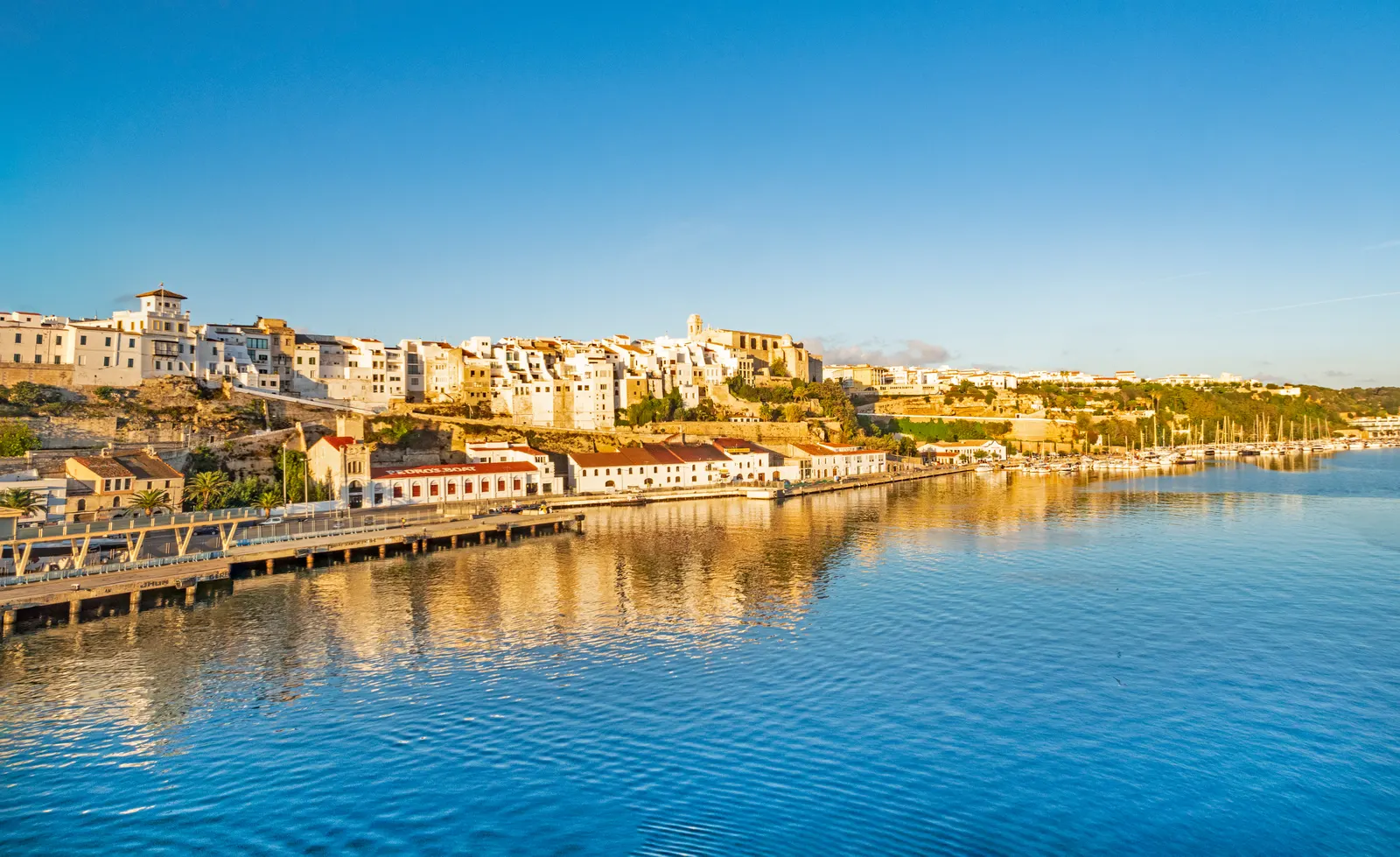 El gran puerto natural de Maó visto desde el agua, con sus muelles y casas escalonadas, en el este de Menorca.