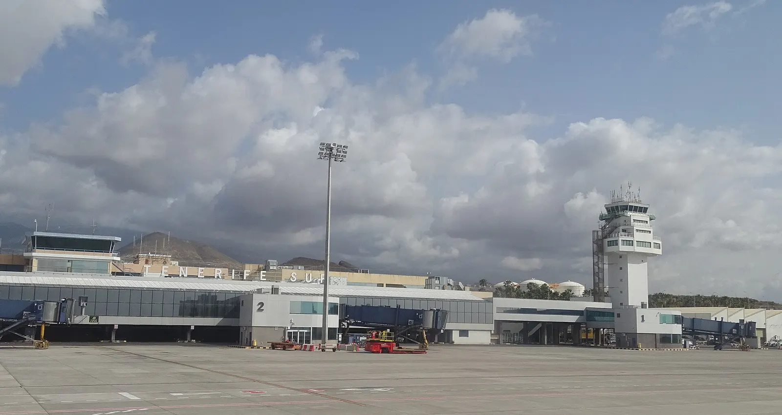 La terminal del aeropuerto de Tenerife Sur y su torre de control, bajo un cielo de nubes blancas.