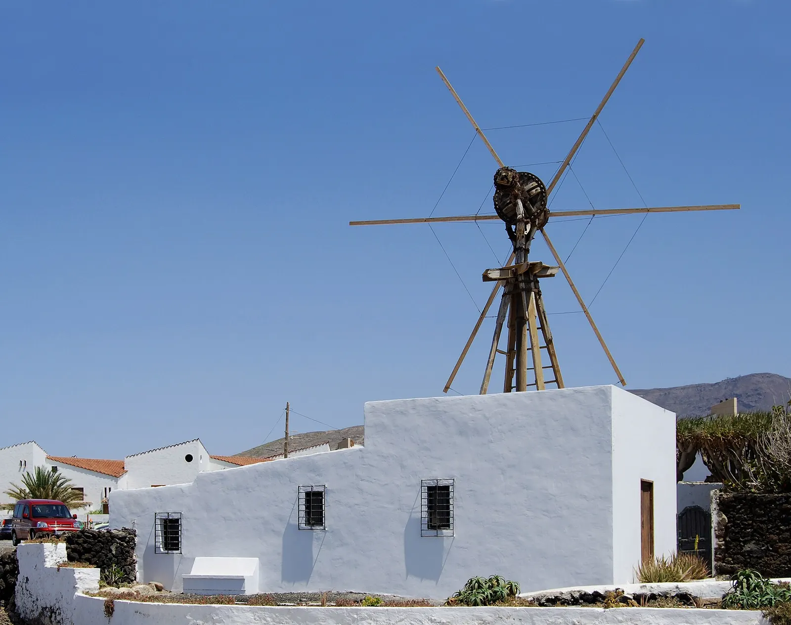 Un molino de viento canario de aspas de madera sobre una casa encalada en el Puerto de las Nieves, con montañas al fondo.