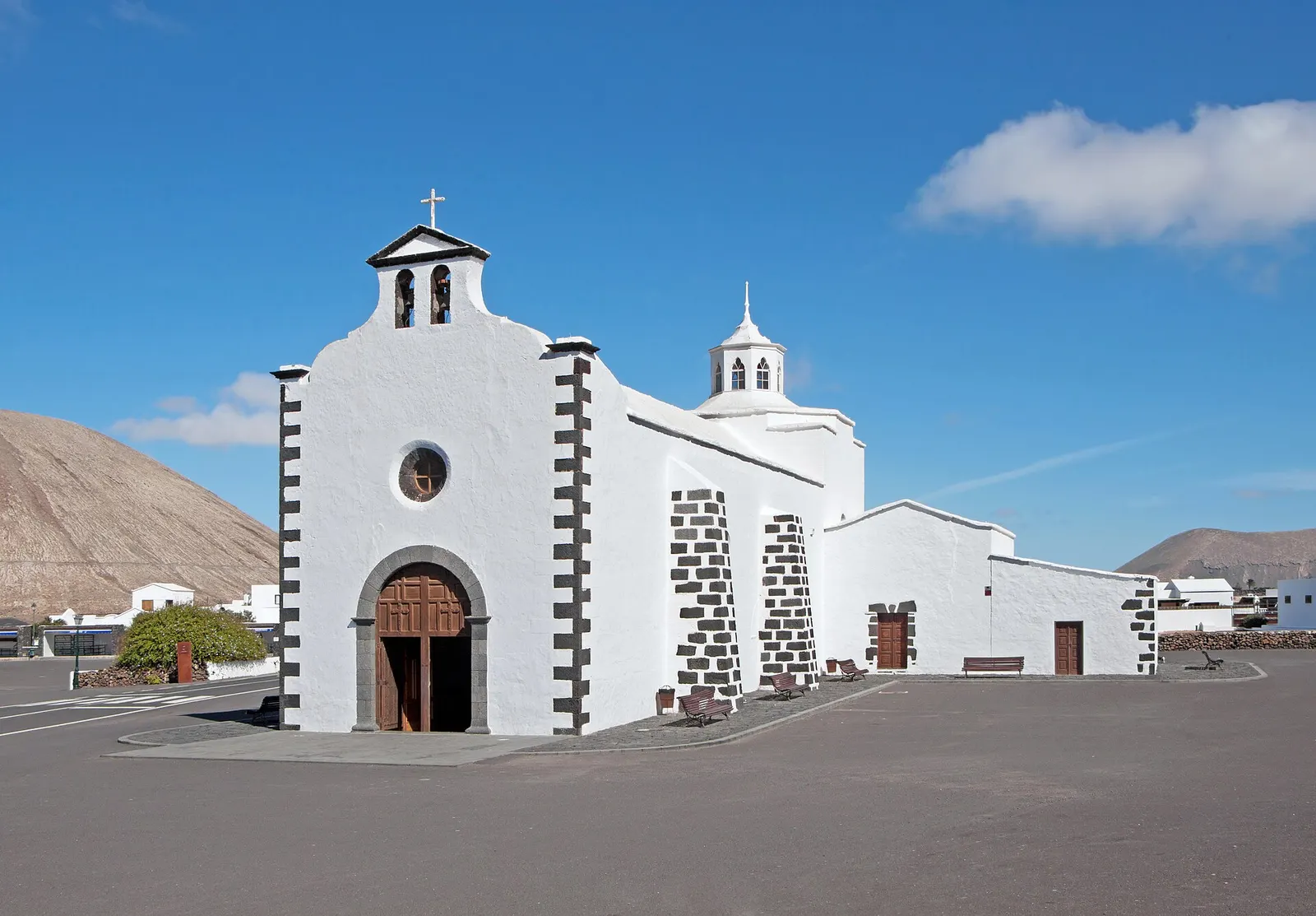 Die weiße Wallfahrtskirche Los Dolores in Mancha Blanca mit Ecken aus Vulkanstein unter blauem Himmel.