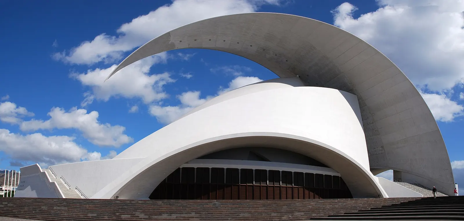 La gran vela de hormigón blanco del Auditorio de Tenerife curvándose sobre la sala, bajo un cielo azul con nubes.