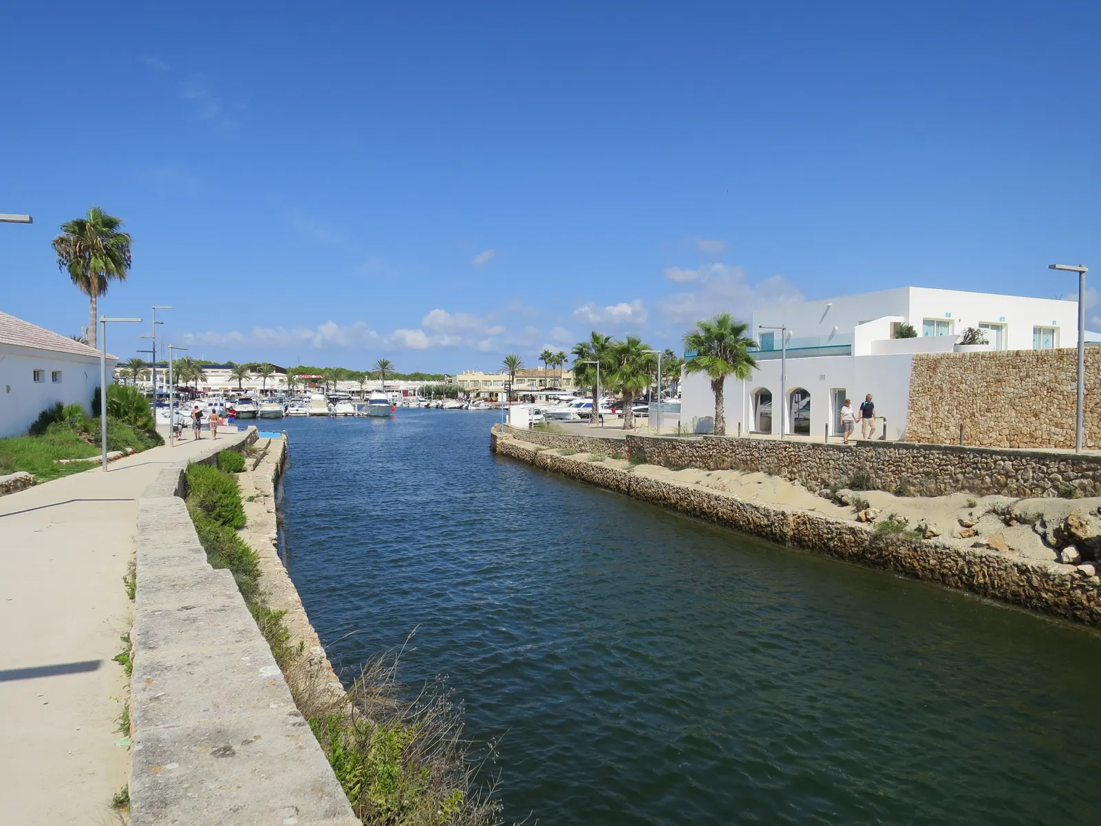 El canal de la marina de Cala en Bosc, con un paseo junto al agua en calma.