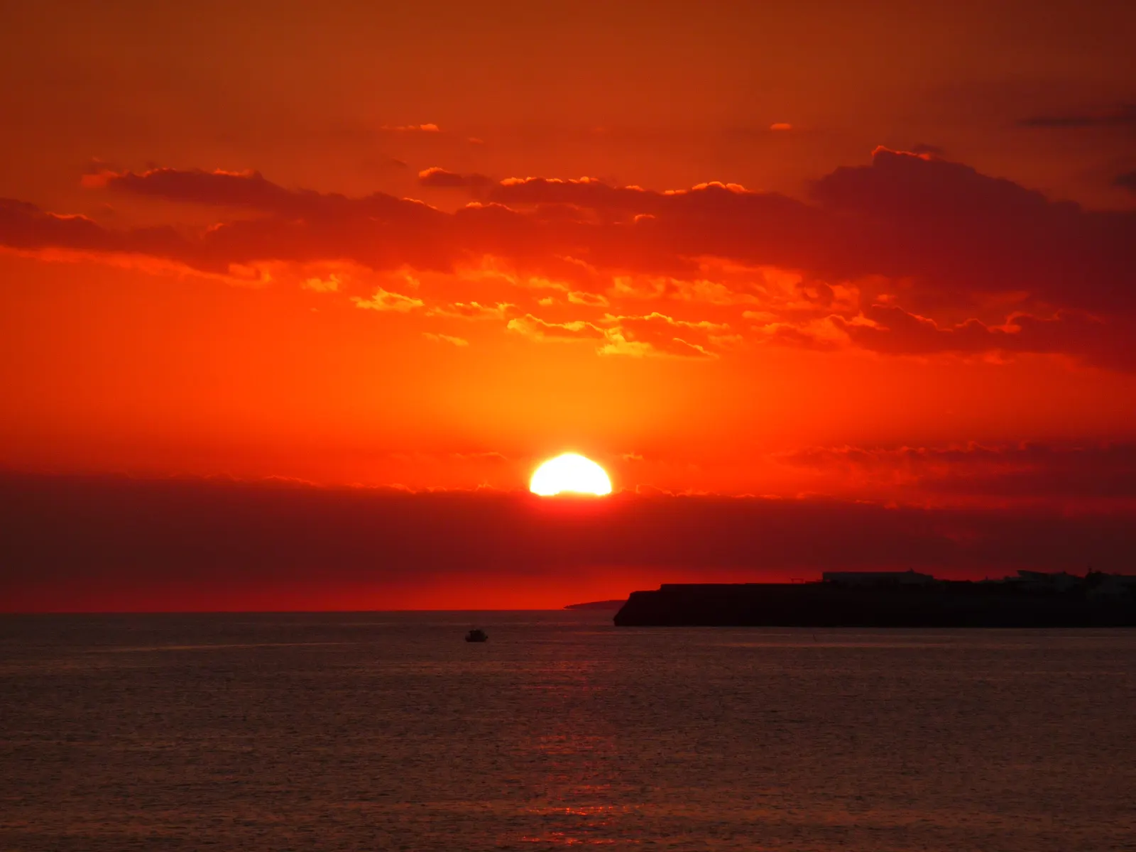 Un atardecer intenso sobre el mar en la costa sureste de Menorca, con el sol asomando entre nubes bajas.