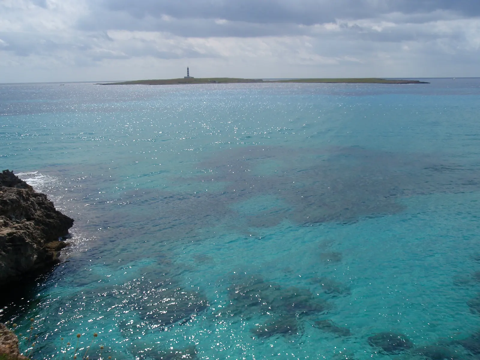 El mar turquesa y transparente frente a Punta Prima, con el islote de l'Illa de l'Aire y su faro al fondo.