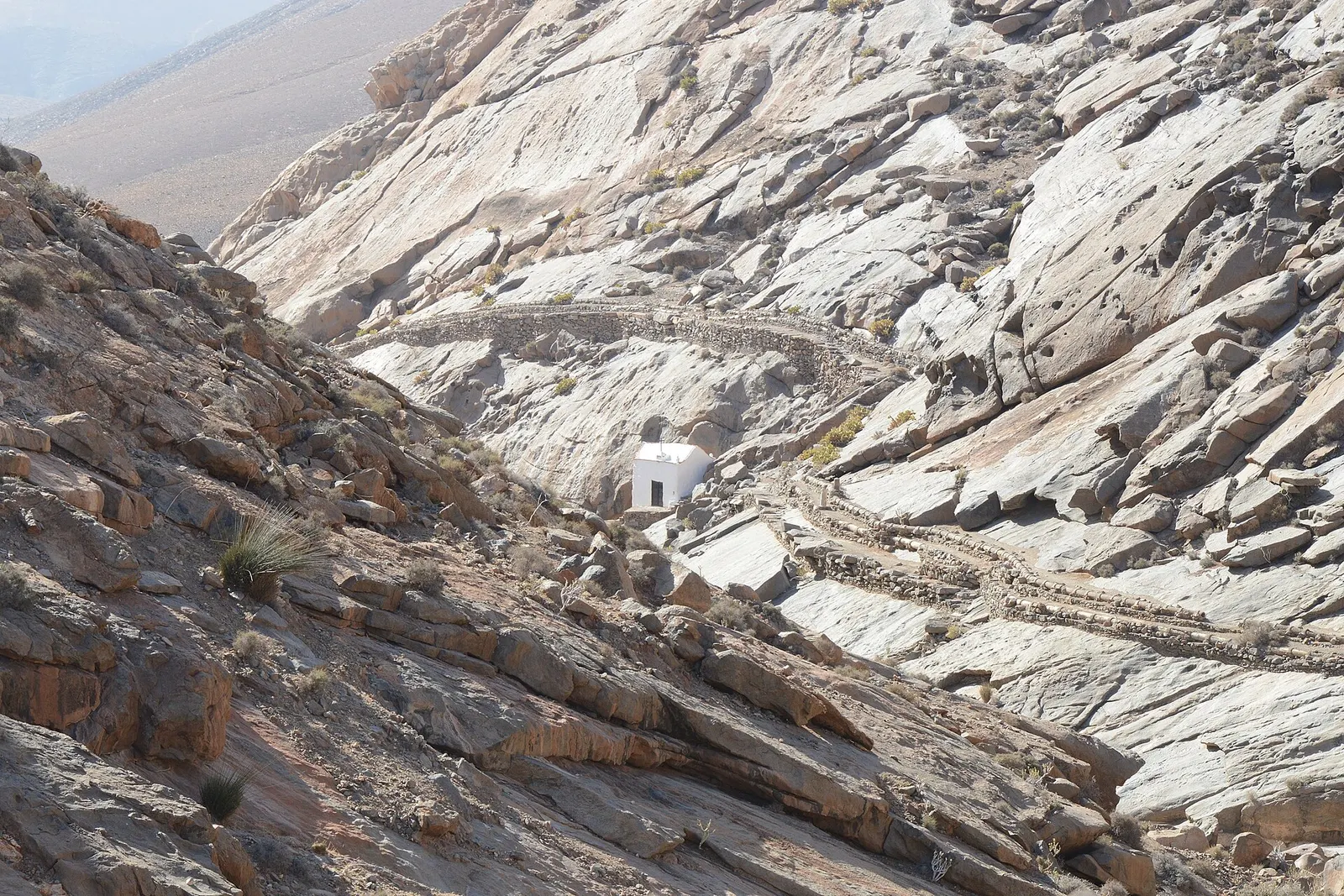 Il piccolo eremo bianco spunta tra le rocce levigate del burrone di las Peñitas, con il vecchio canale scavato nel pendio.