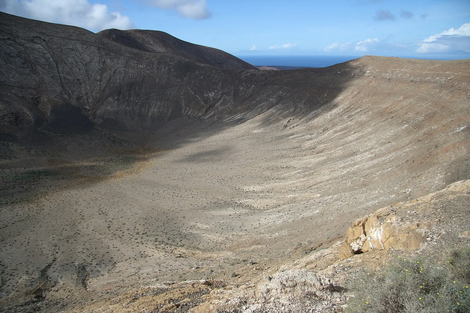 Inside Caldera Blanca seen from its rim: a wide, pale crater with the ocean appearing beyond.