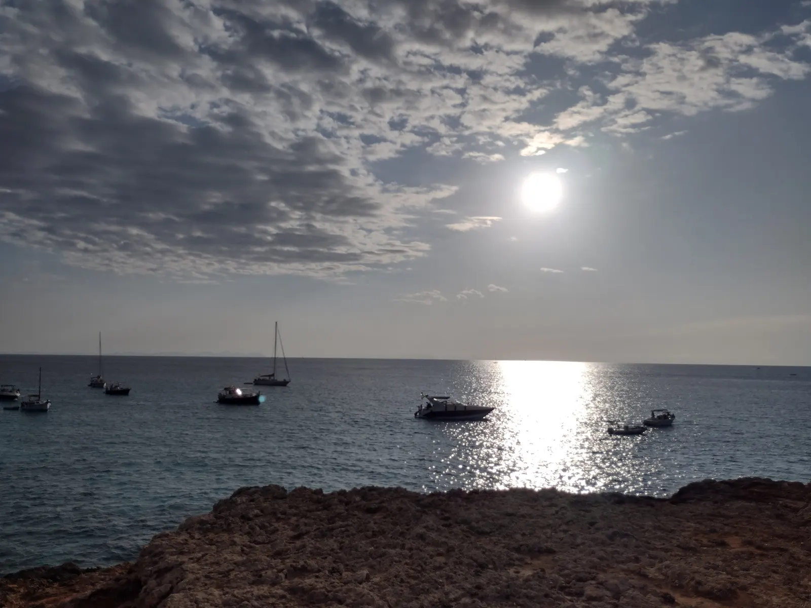 Barcas fondeadas en una cala de Menorca, con el sol reflejado en el agua en calma al atardecer.