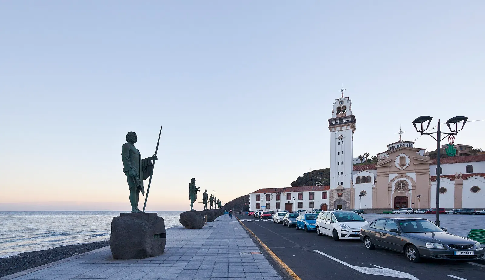 La basílica de Candelaria y su campanario blanco al final del paseo marítimo, junto a las estatuas de los menceyes frente al mar.