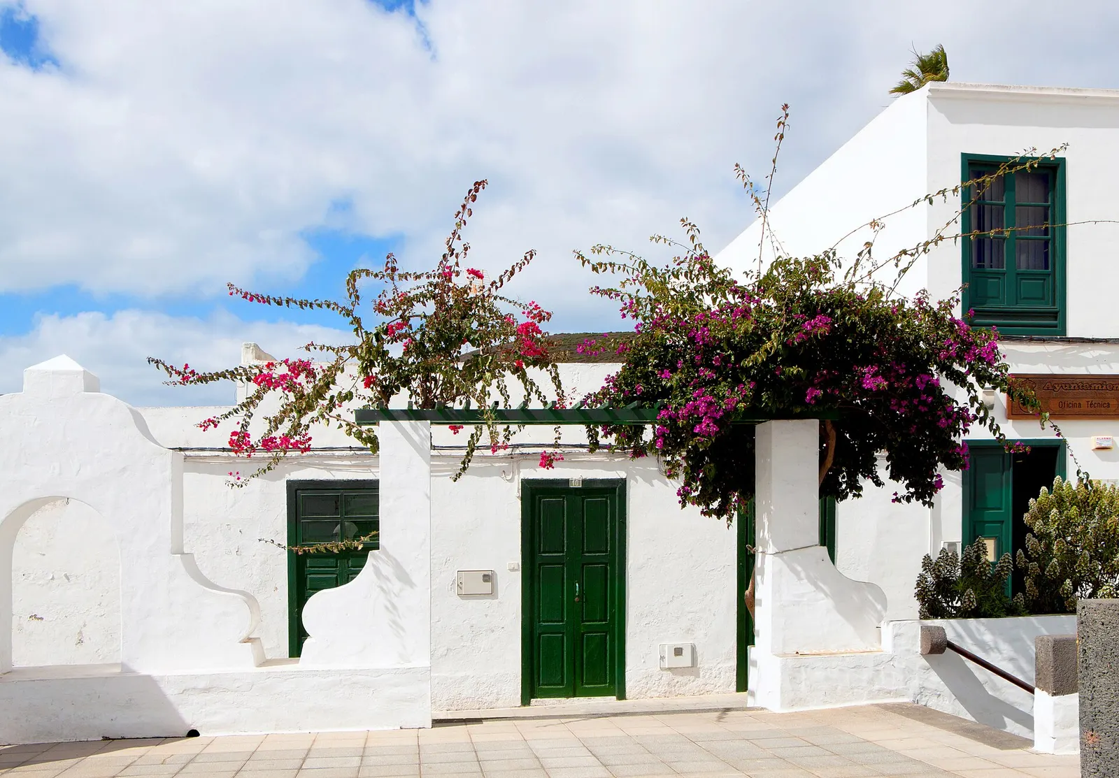 Una casa encalada de Haría con puertas y ventanas verdes y una buganvilla en flor sobre el muro.