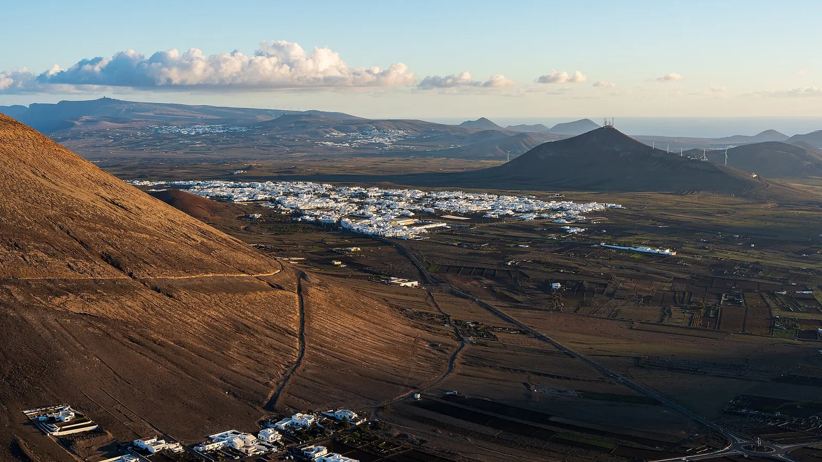 Los pueblos blancos de San Bartolomé se extienden sobre la llanura volcánica a primera hora, con volcanes y nubes al fondo.