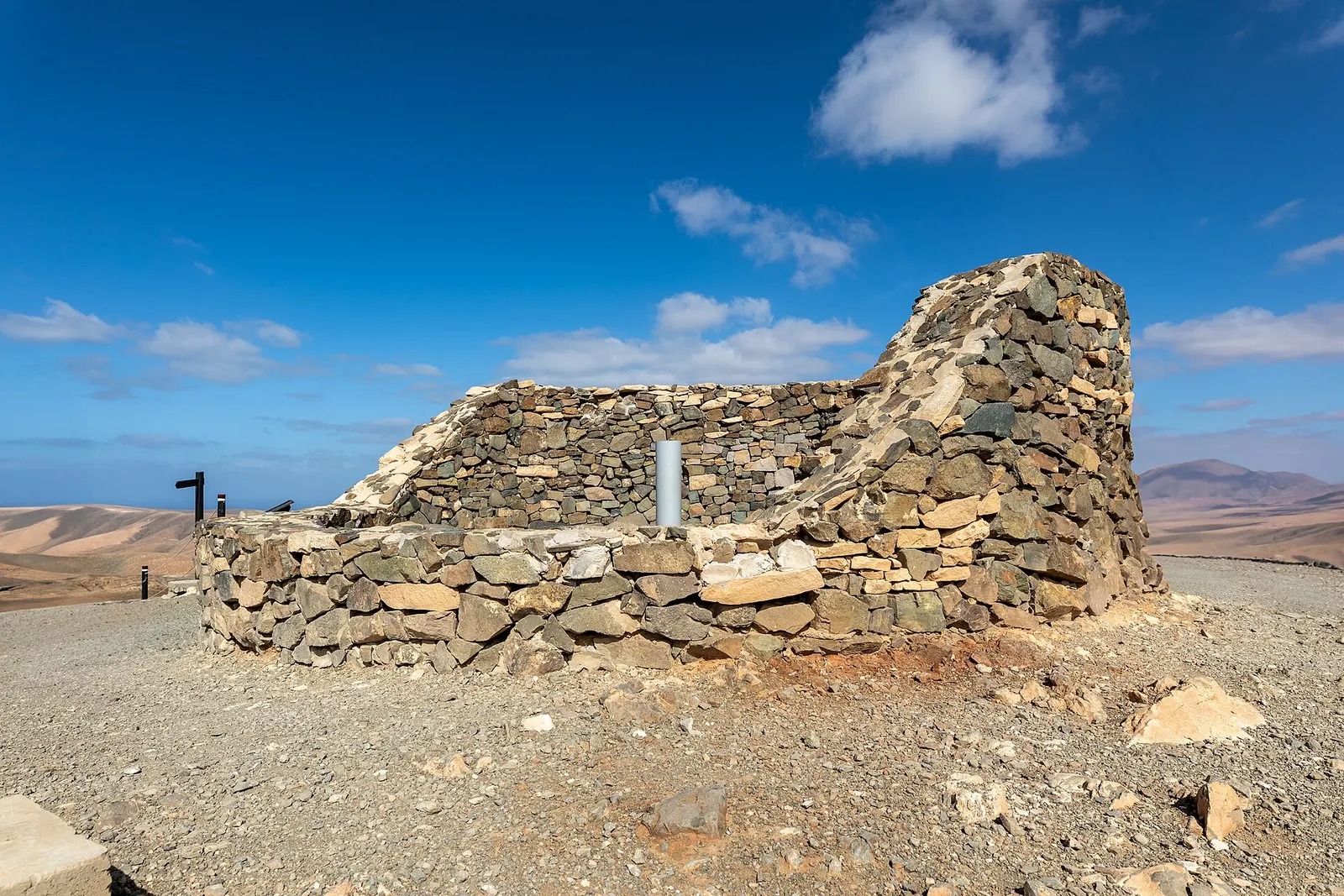 El mirador astronómico de Sicasumbre, un muro curvo de piedra seca sobre la cumbre, con lomas áridas y cielo abierto alrededor.
