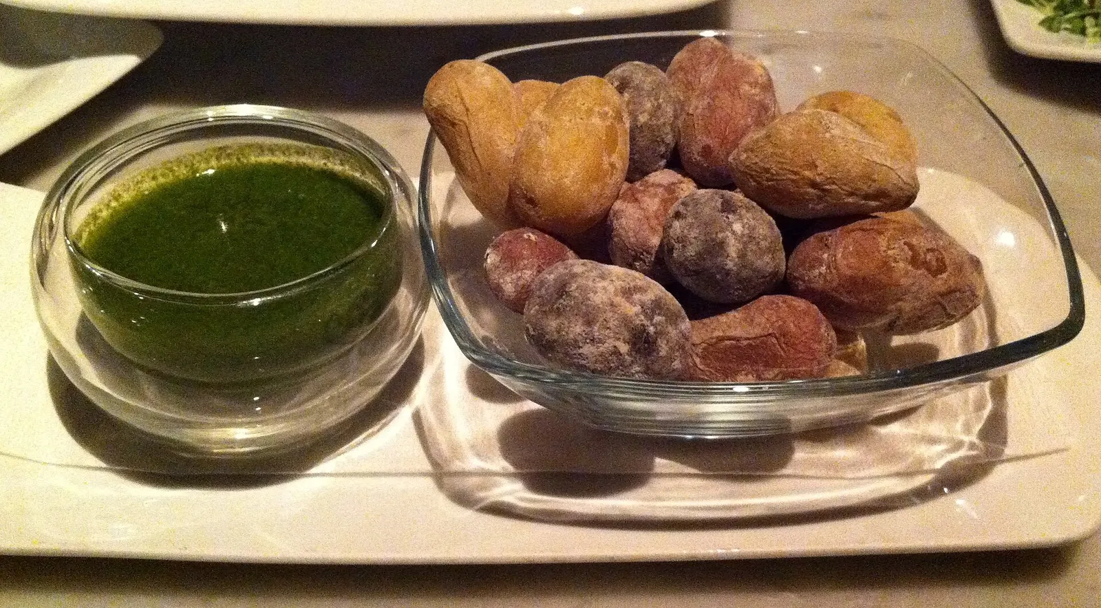 Papas arrugadas con su costra de sal junto a un cuenco de mojo verde, servidas sobre cristal.