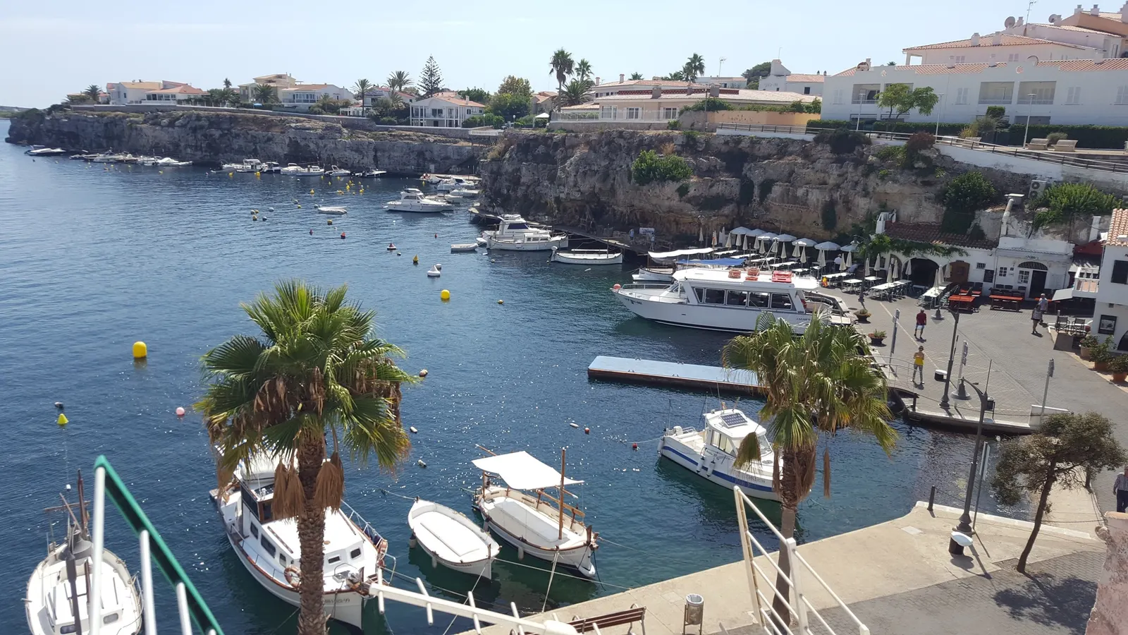 Cales Fonts, en Es Castell, con casas sobre el acantilado y embarcaciones amarradas en el puerto natural.