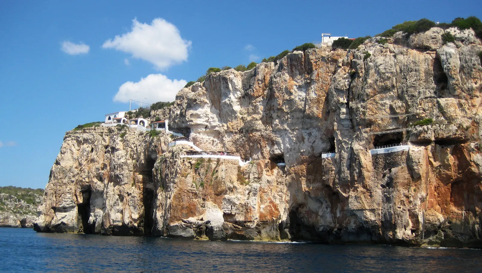 El acantilado de Cova d'en Xoroi visto desde el mar, con las terrazas blancas excavadas en la roca.