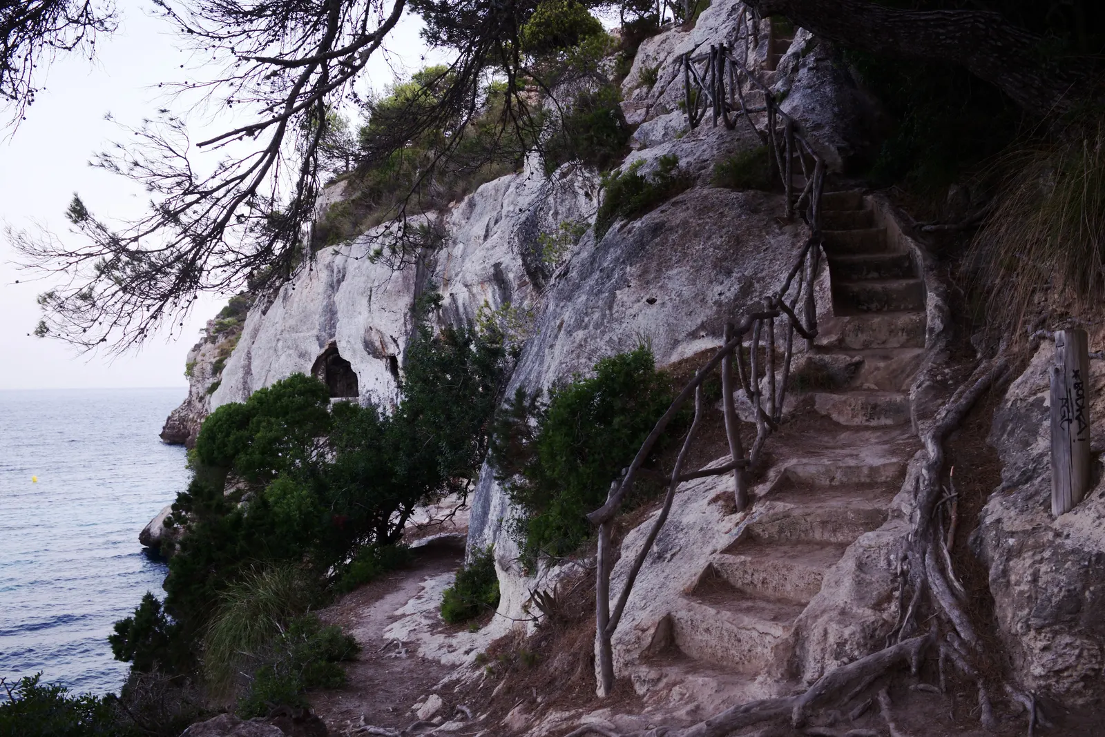 Un sendero de piedra tallado en el acantilado, bajando hacia el mar en algún punto de la costa de Menorca.