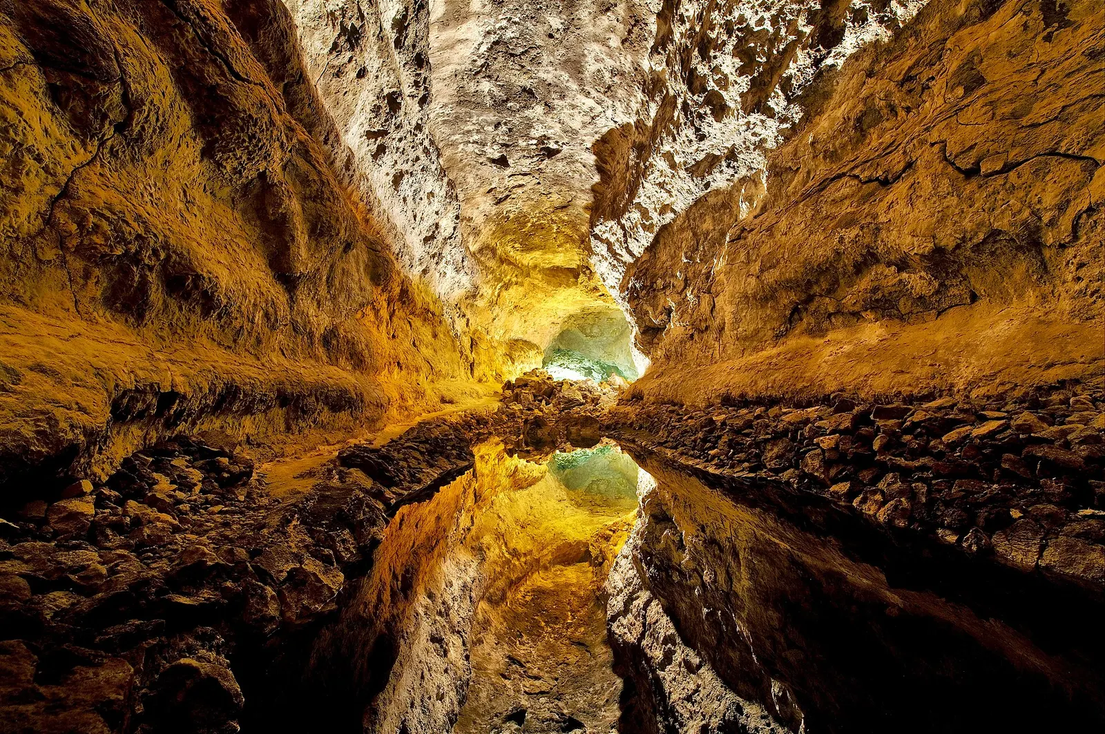 Las paredes doradas de la galería de lava se reflejan en un agua inmóvil que parece duplicar la cueva.