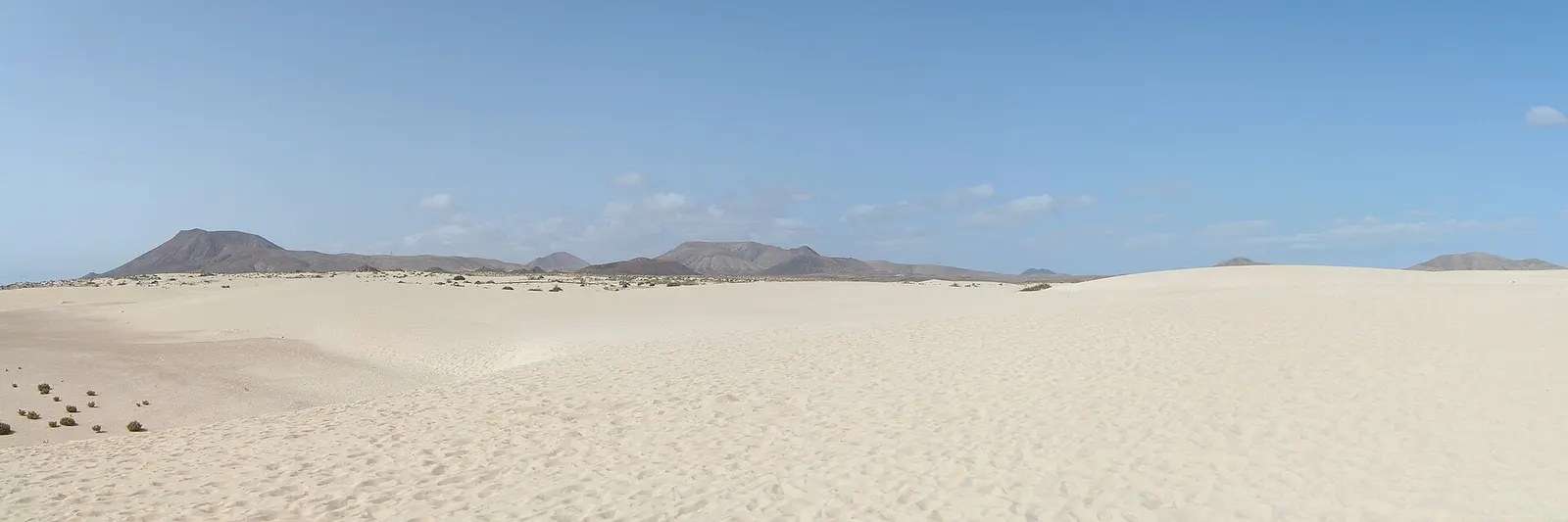 Una llanura de arena blanca y casi intacta se extiende hacia las montañas volcánicas del horizonte en las Dunas de Corralejo.