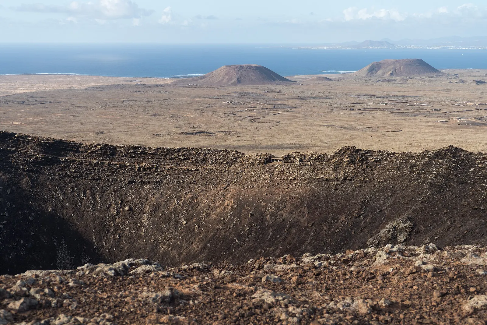 El cráter de Calderón Hondo abre su hondo cuenco de lava, con conos volcánicos, la llanura del norte y el mar detrás.