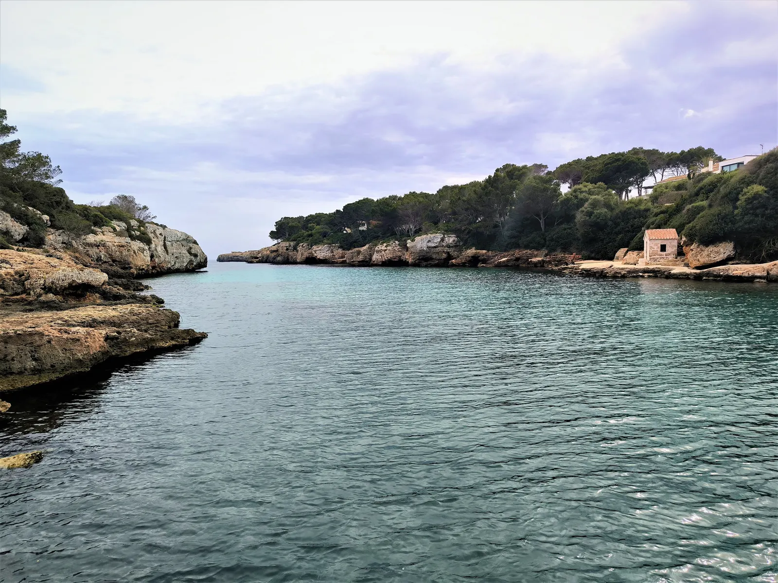 Una cala estrecha de agua turquesa junto a Ciutadella, entre paredes de roca caliza cubiertas de pinos.
