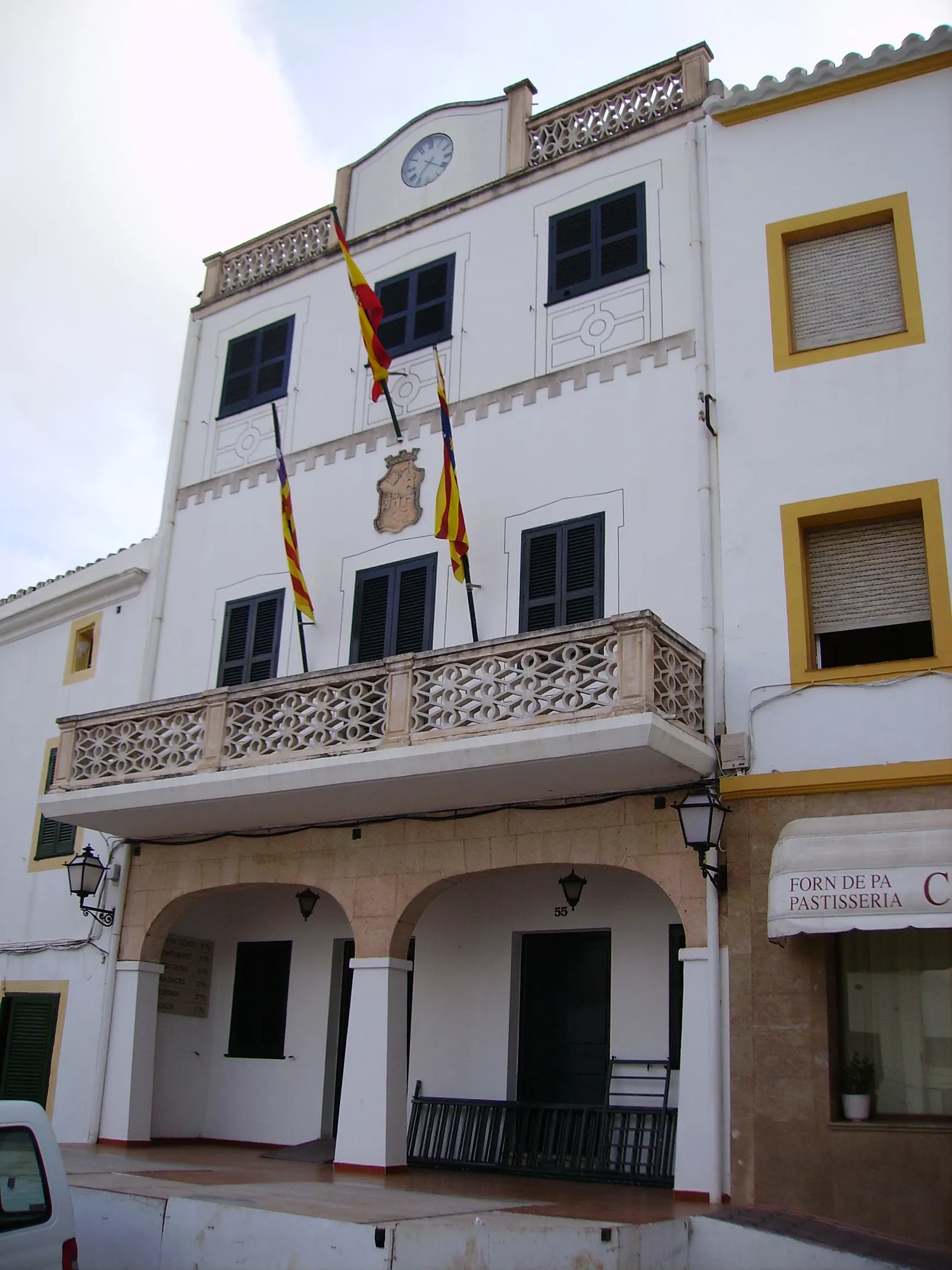 La fachada del ayuntamiento de Ferreries, con sus banderas y un obrador de pan en los bajos.