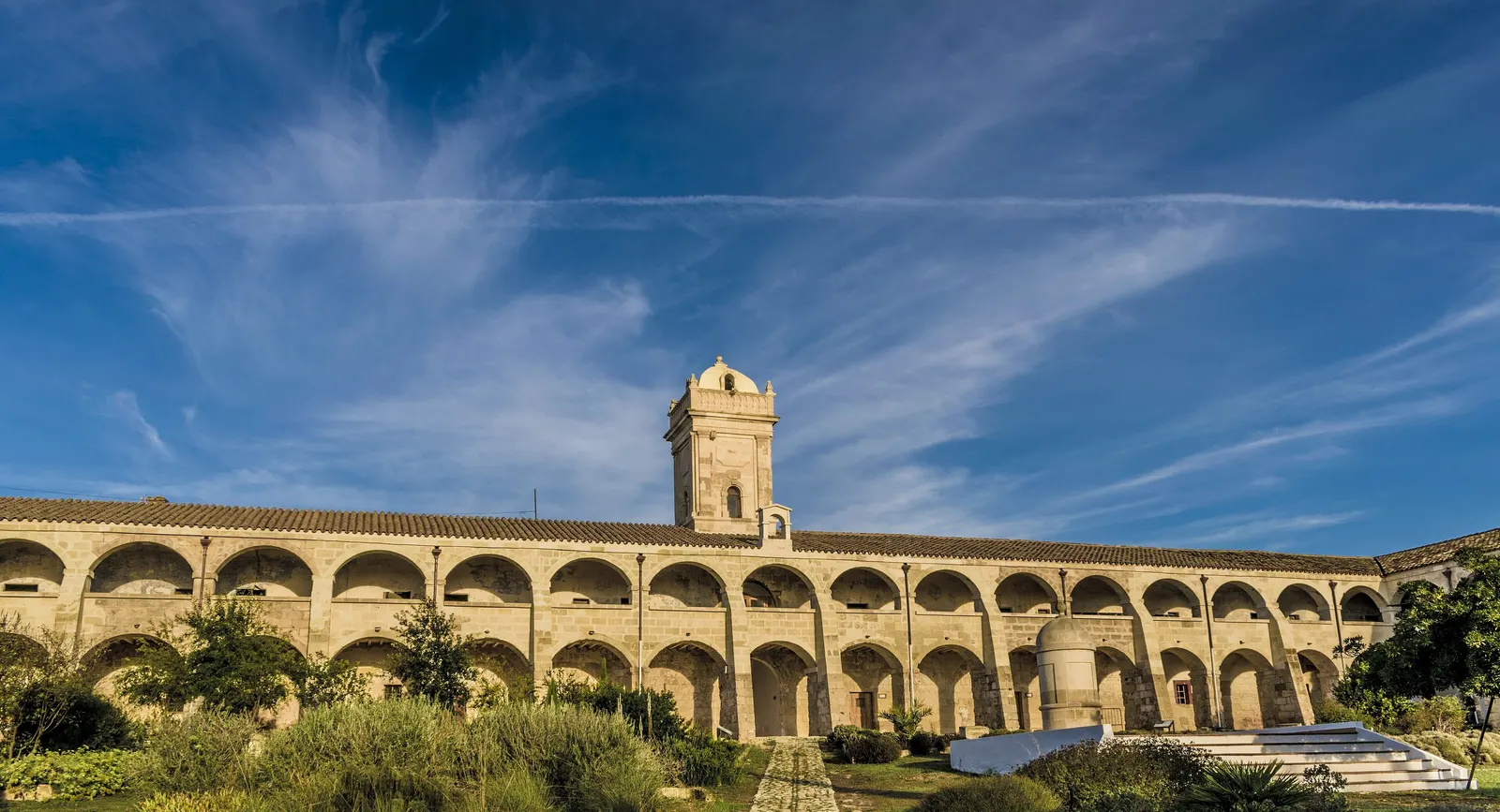 El claustro porticado del antiguo hospital naval de la Illa del Rei, con su torre y el jardín delante.