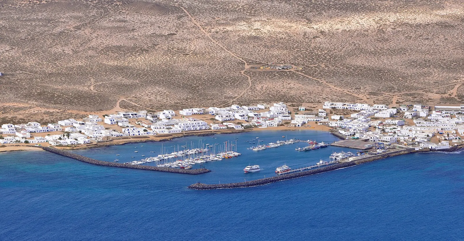Caleta del Sebo desde lo alto: casas blancas junto al puerto y pistas de arena que cruzan la isla.