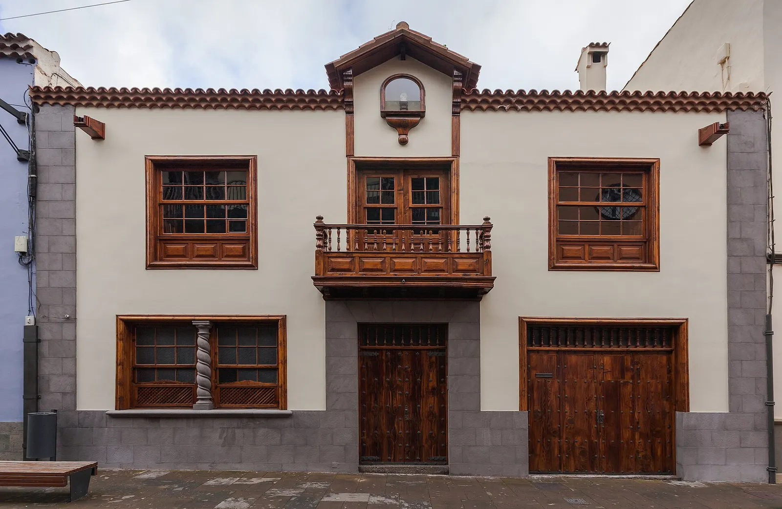 Fachada encalada de una casa tradicional de La Laguna, con balcón y ventanas de madera y piedra gris en el zócalo.