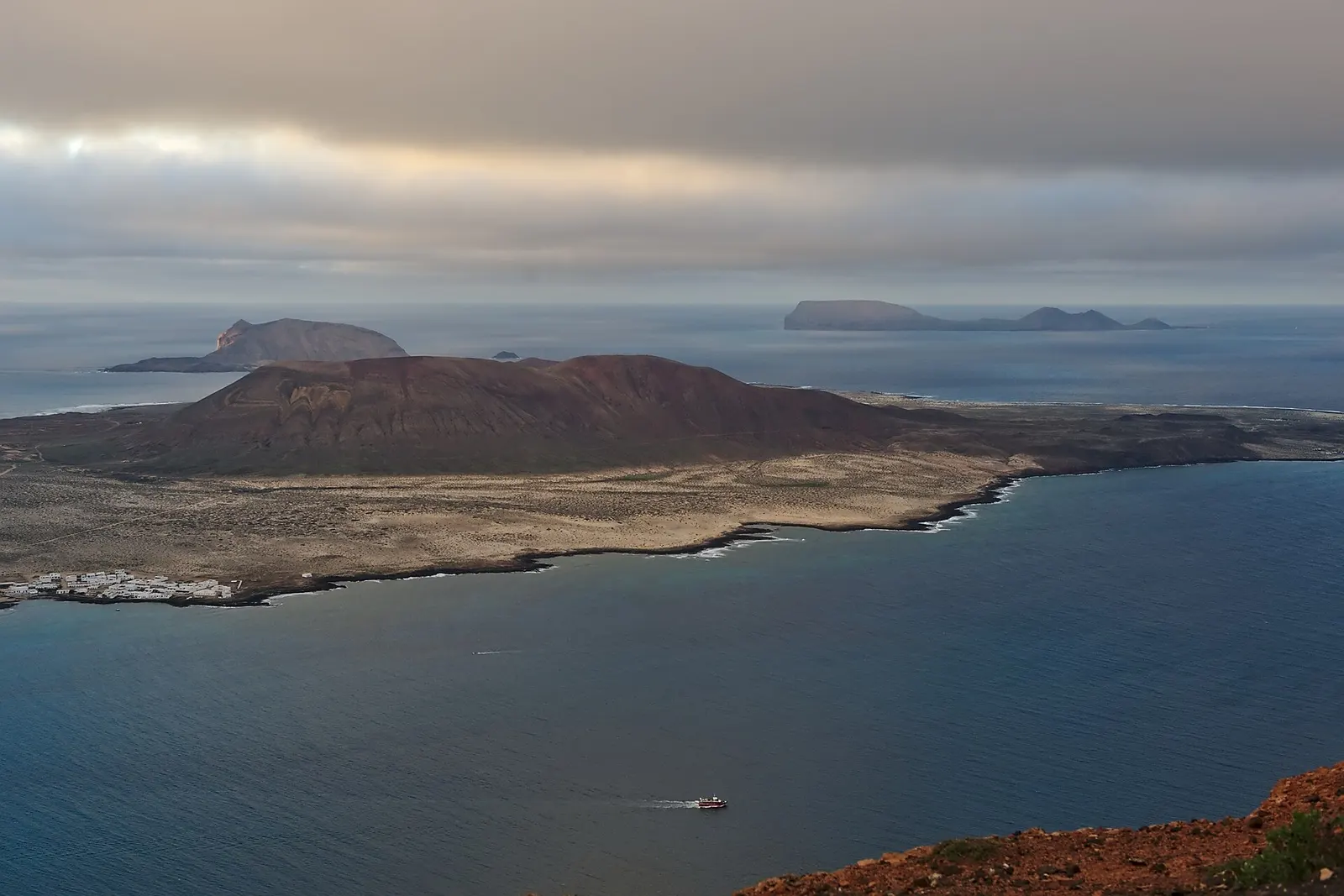 Ein Boot überquert die Meerenge El Río nach La Graciosa, dahinter die Inselchen des Chinijo-Archipels.