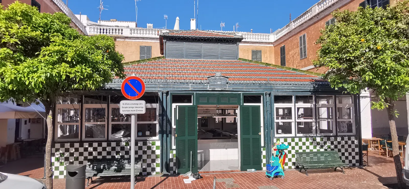 La pescheria della Plaça de la Llibertat, a Ciutadella, con la facciata piastrellata bianca e verde e le persiane coordinate, incorniciata da due aranci.