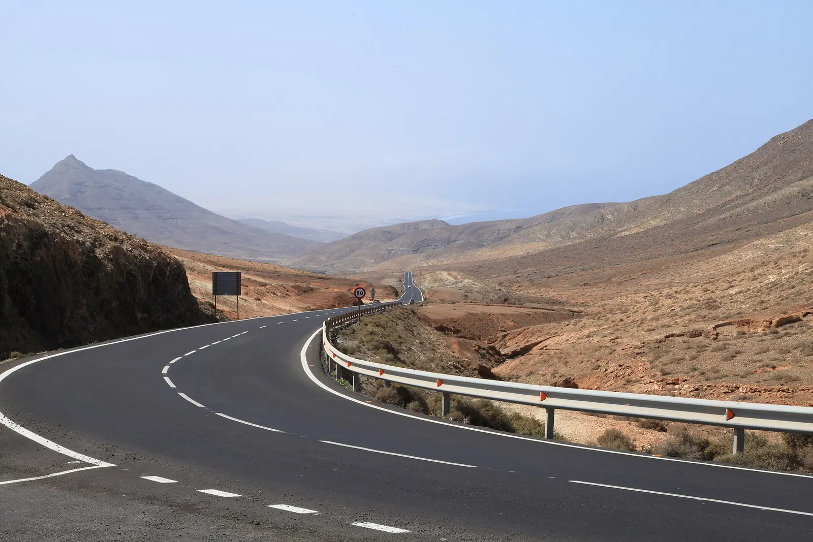Una carretera vacía traza una curva entre montañas áridas de tonos ocres en el interior de Pájara.
