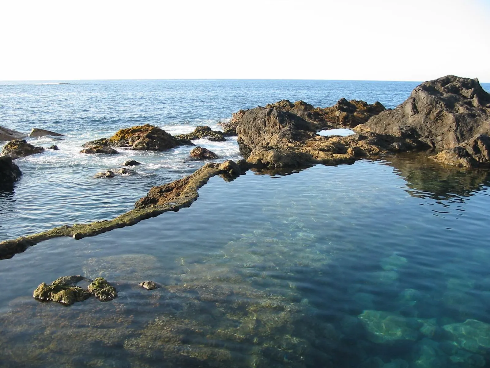 Una poza de agua transparente entre rocas volcánicas en El Caletón de Garachico, con el Atlántico detrás.