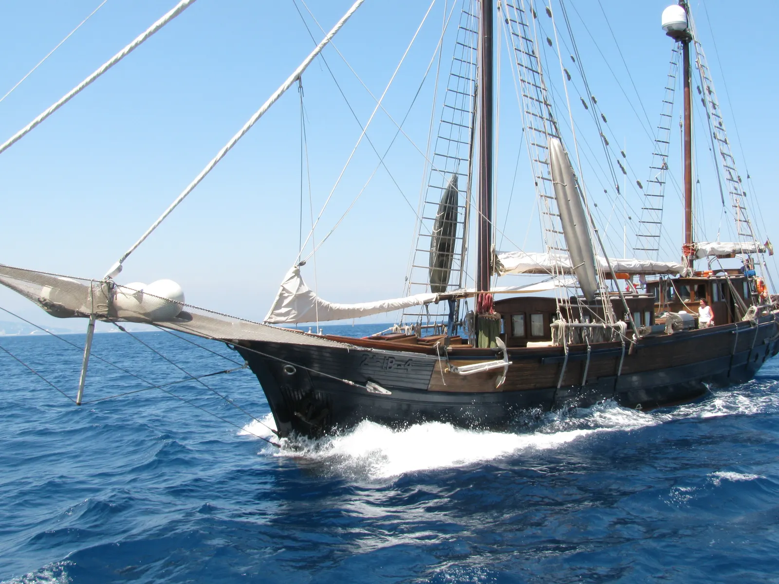 Una barca a vela classica in legno naviga a vele spiegate su acque blu, durante una regata.