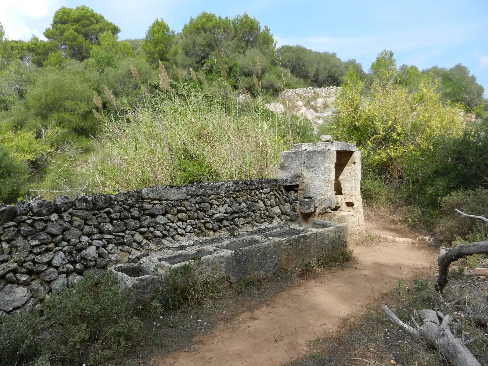 Uma fonte e um muro de pedra seca ao longo de um caminho rural perto de Es Migjorn Gran.