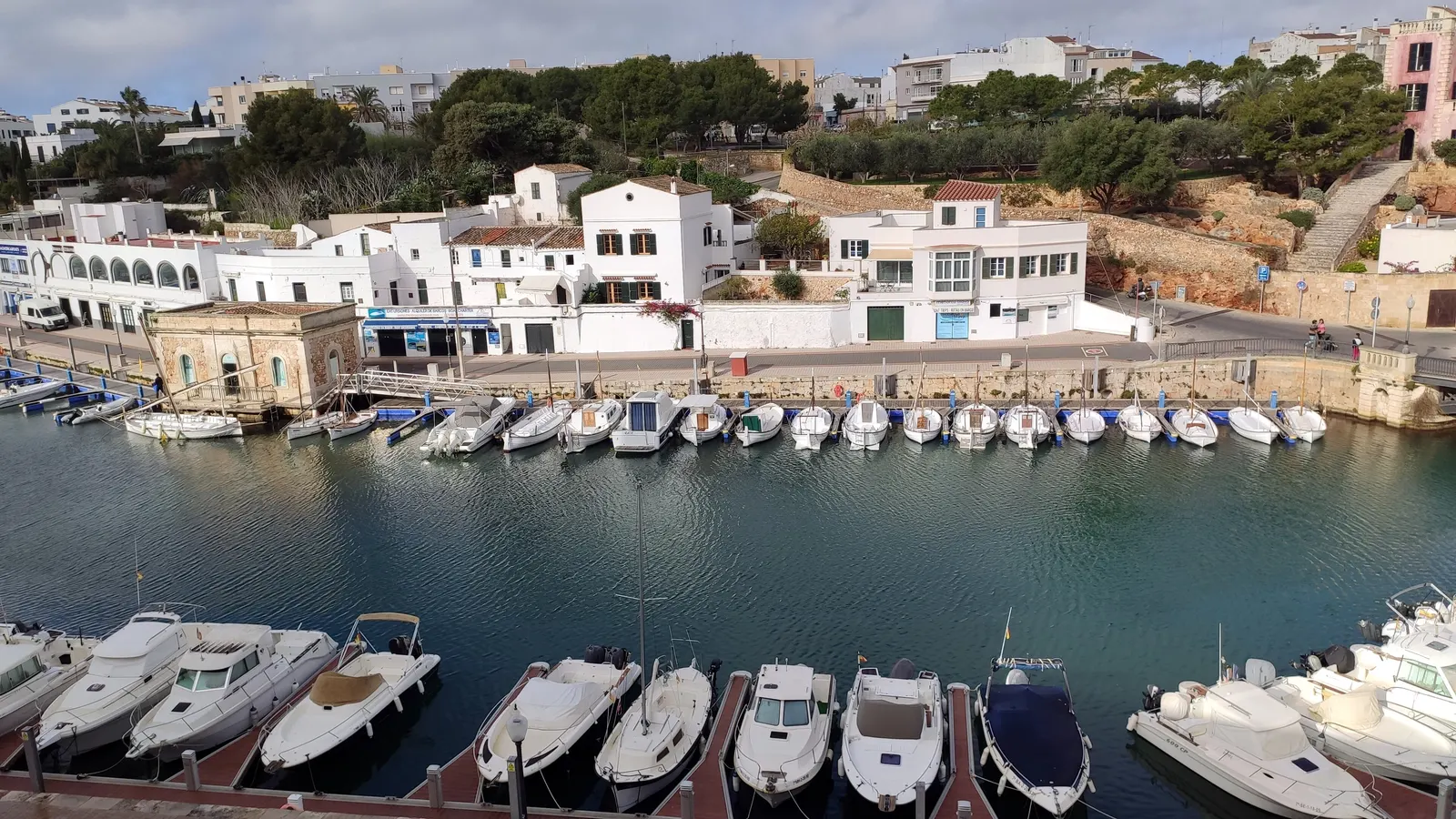 O porto de Ciutadella visto do alto, com os barcos amarrados em fila e casas brancas junto ao cais