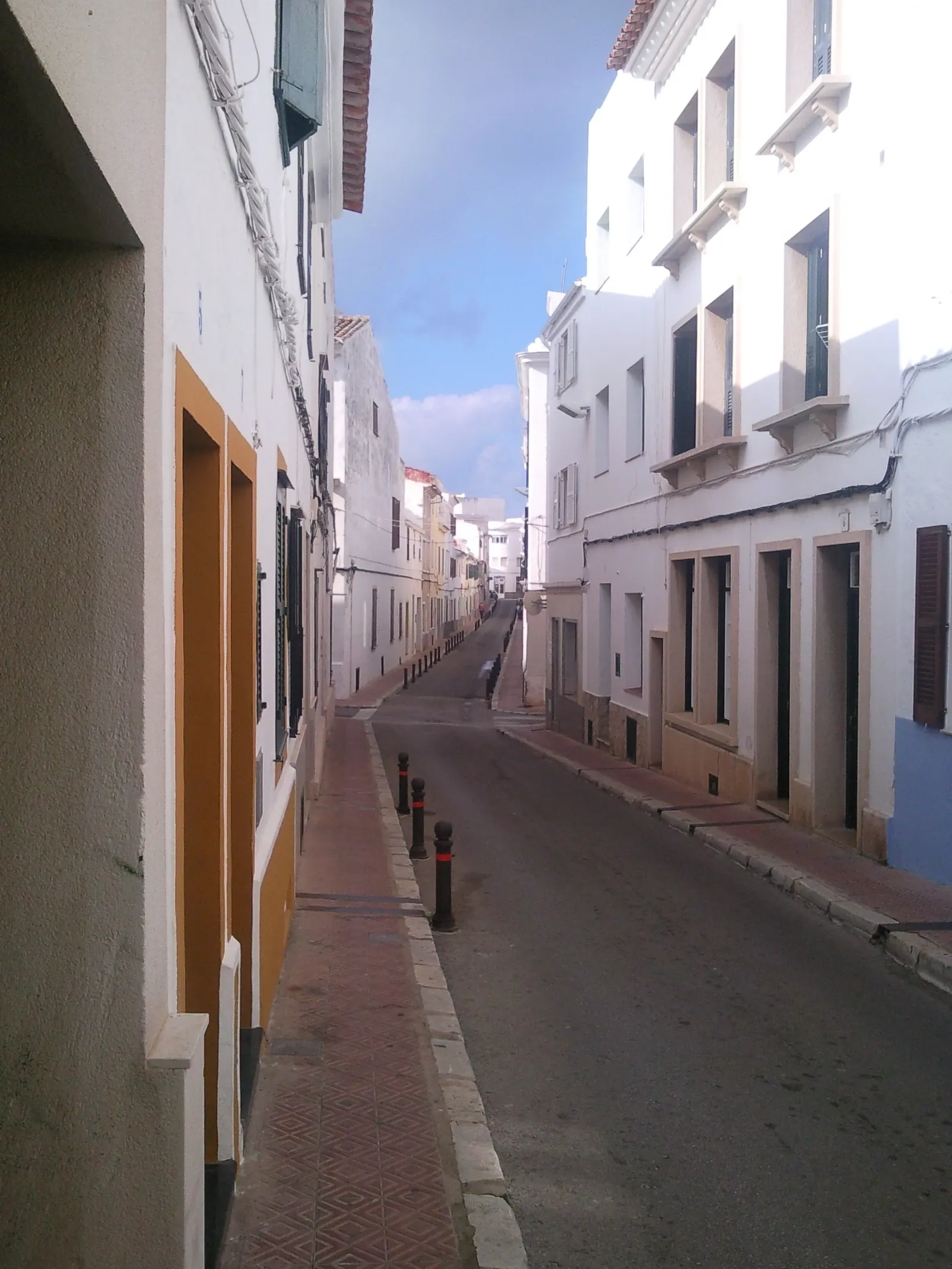 Uma rua tranquila e vazia do centro histórico de Maó, com fachadas coloridas ao entardecer.