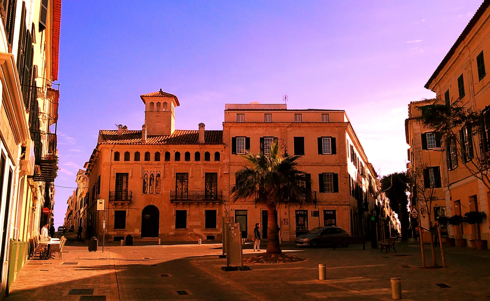 A Plaça Princep, vazia ao entardecer, com as suas fachadas de pedra e uma palmeira, no centro histórico de Maó.