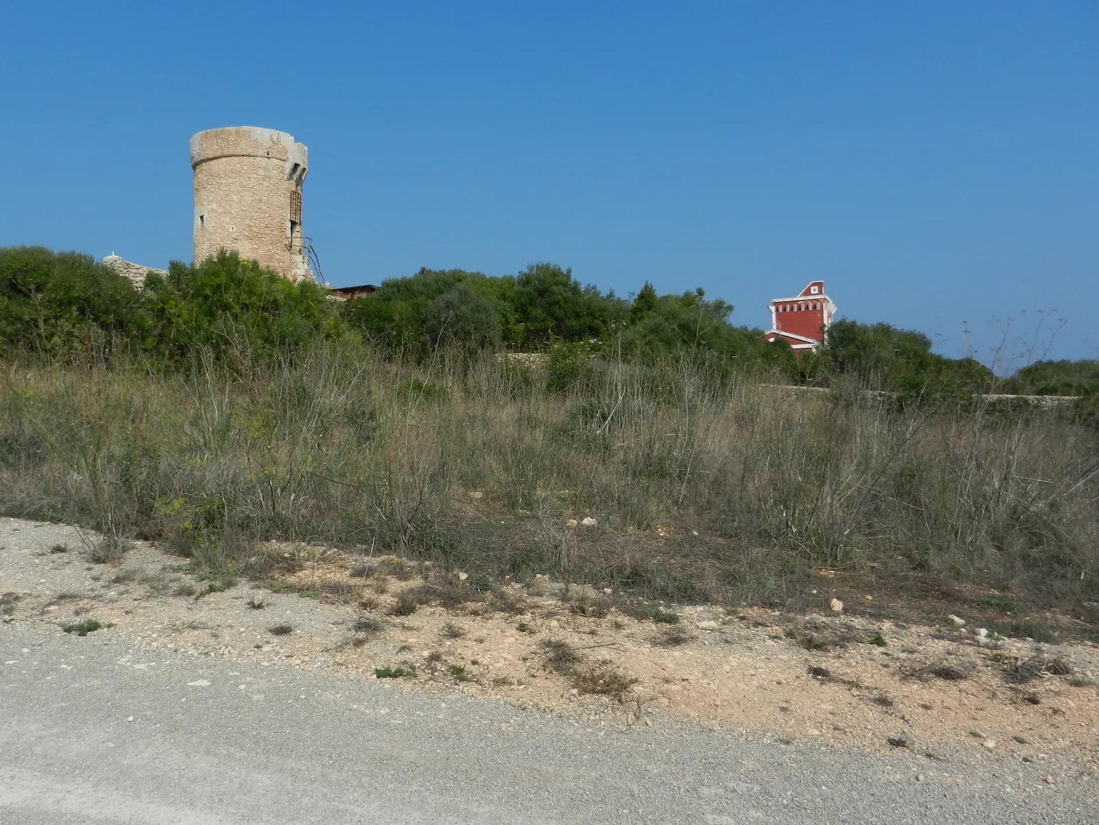 A torre de Torret, entre o campo e uma casa de telhado vermelho, no interior rural de Sant Lluís.