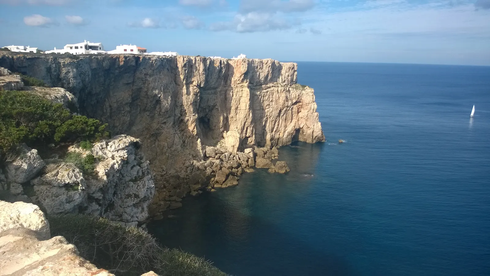 El acantilado de Cala Morell, piedra caliza dorada cayendo sobre un mar azul intenso.