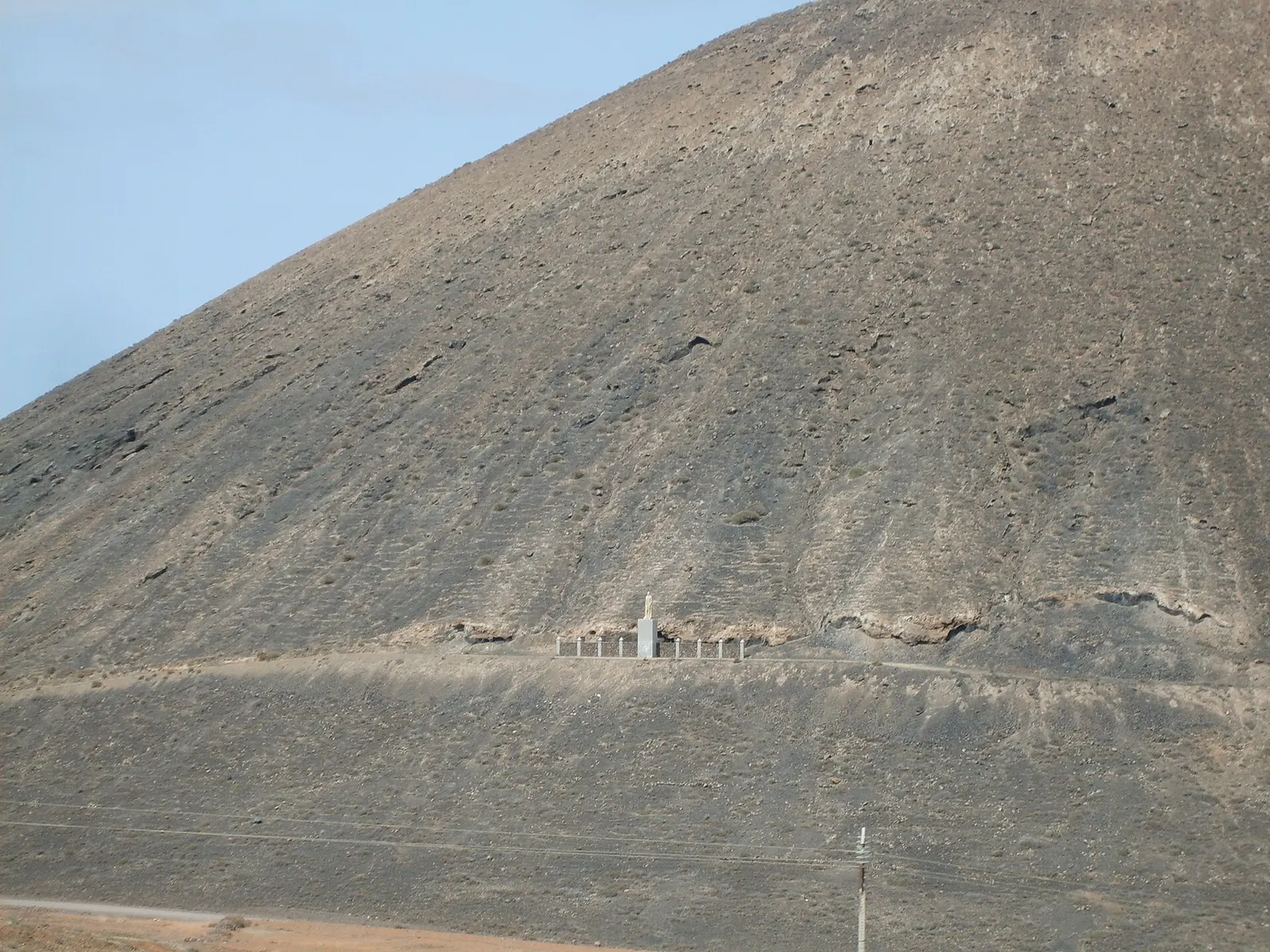 La ladera oscura de Montaña Quemada, con el pequeño monumento blanco a Unamuno a media altura y el cielo pálido detrás.