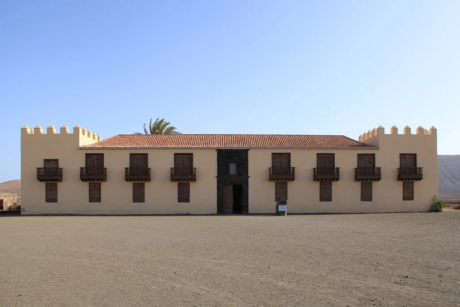 La fachada encalada de la Casa de los Coroneles en La Oliva, con sus torres almenadas y balcones de madera bajo un cielo limpio.