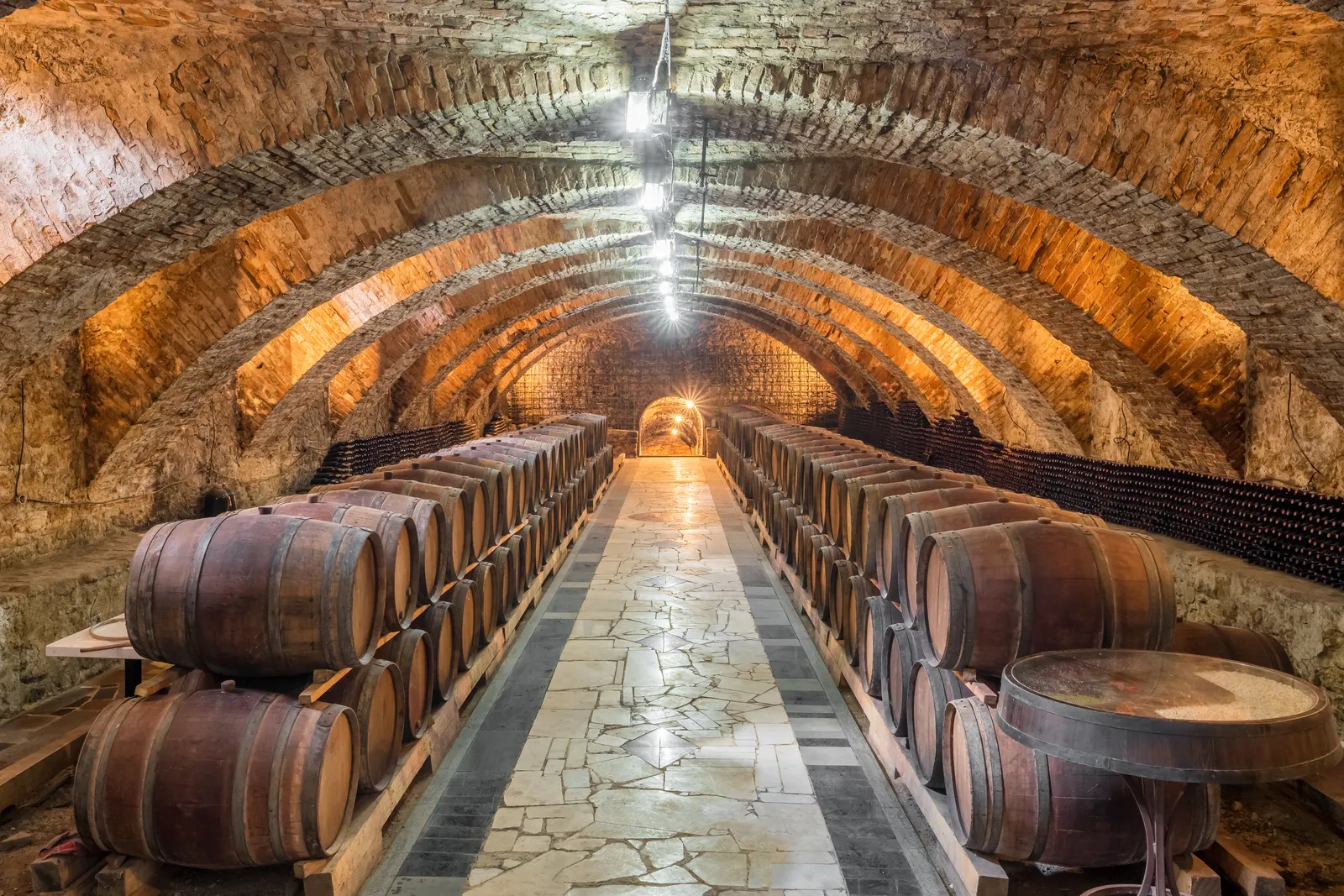 Vaulted cellar with rows of oak barrels ageing wine in the dim light.